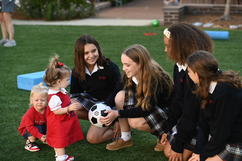 A group of girls in uniform kneeling on grass with a soccer ball